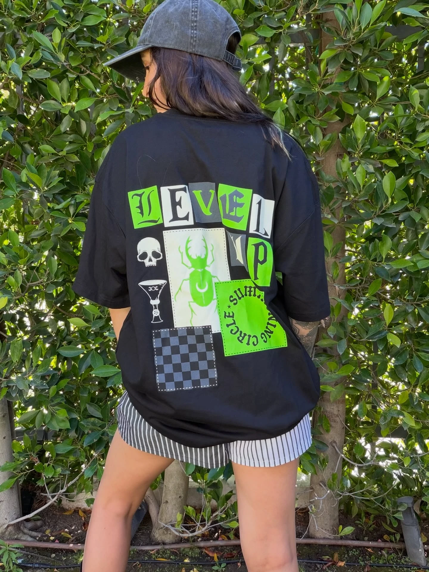 Back view of Level Up in the oversized black Summoning Circle tee with a green beetle, skull and cut-out Level Up lettering
